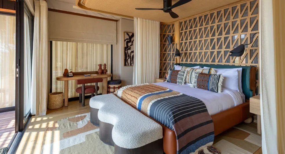 A suite bedroom at Anantara Tented Camp Kafue River pairs patterned textiles with warm wood.