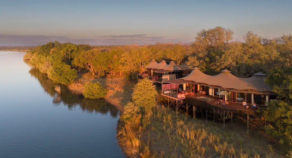 Tented suites at Anantara Tented Camp Kafue River trail along a golden riverbank at sunset.
