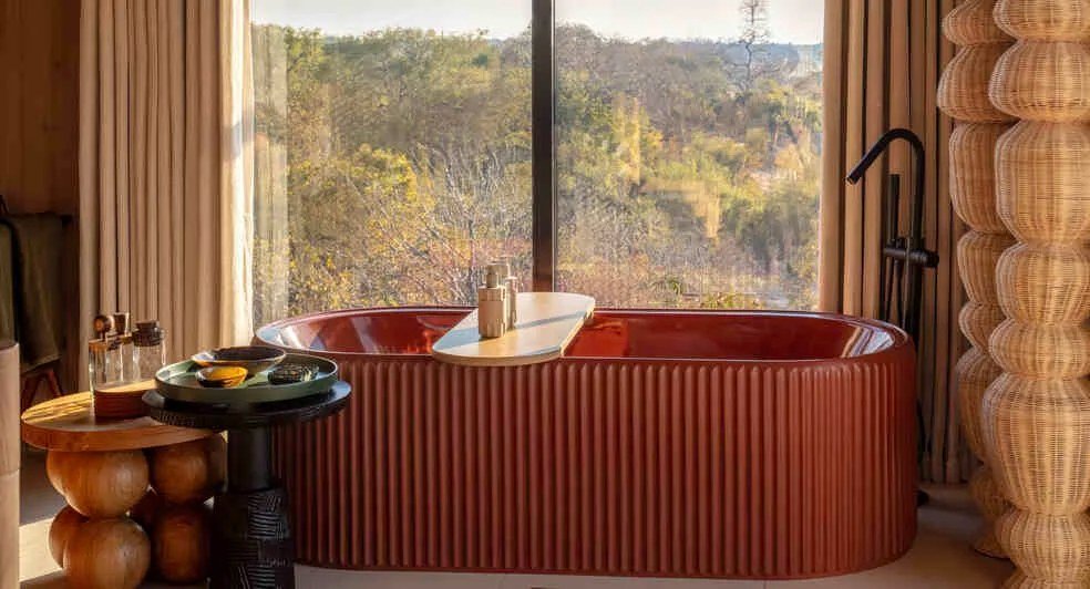 A ribbed, rust-toned tub sits beneath a forest view at Anantara Tented Camp Kafue River.