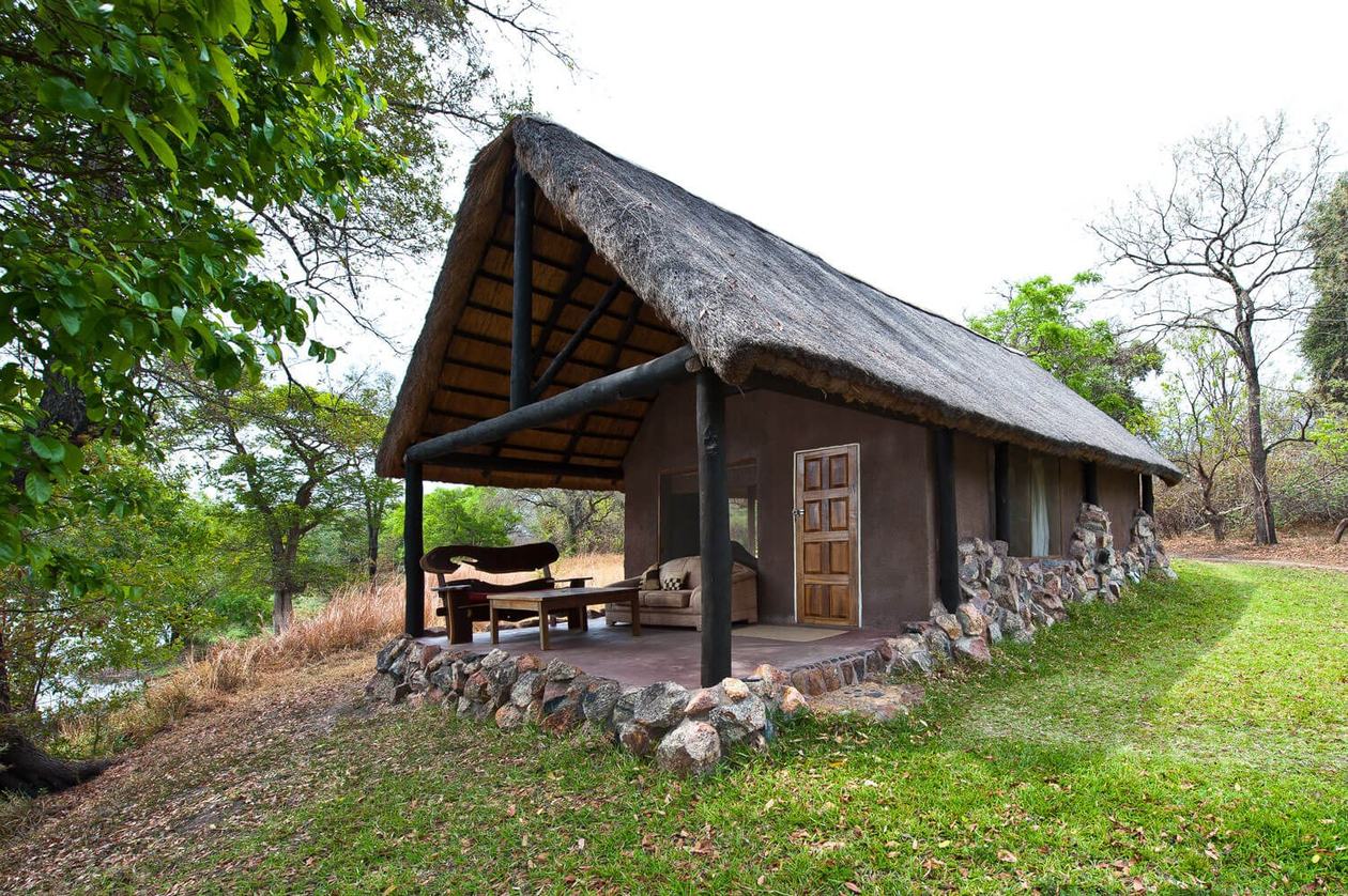 A stone-and-thatch chalet with a covered porch stands at Hippo Lodge in Kafue.