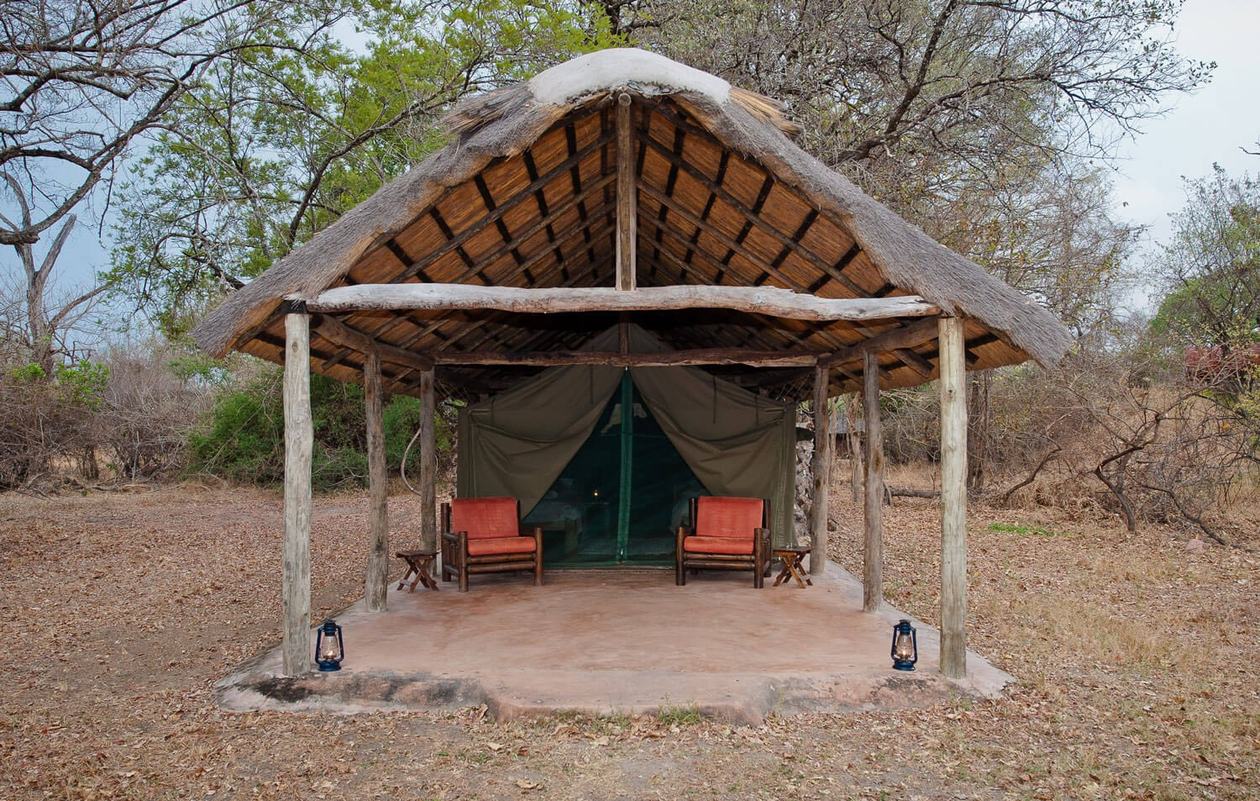 A safari tent with canvas walls sits under a thatched shelter at Hippo Lodge.