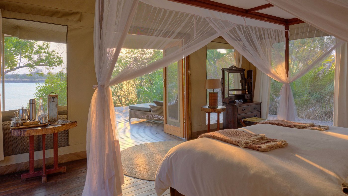 A four-poster bed faces glass doors open to the river at Ila Safari Lodge.