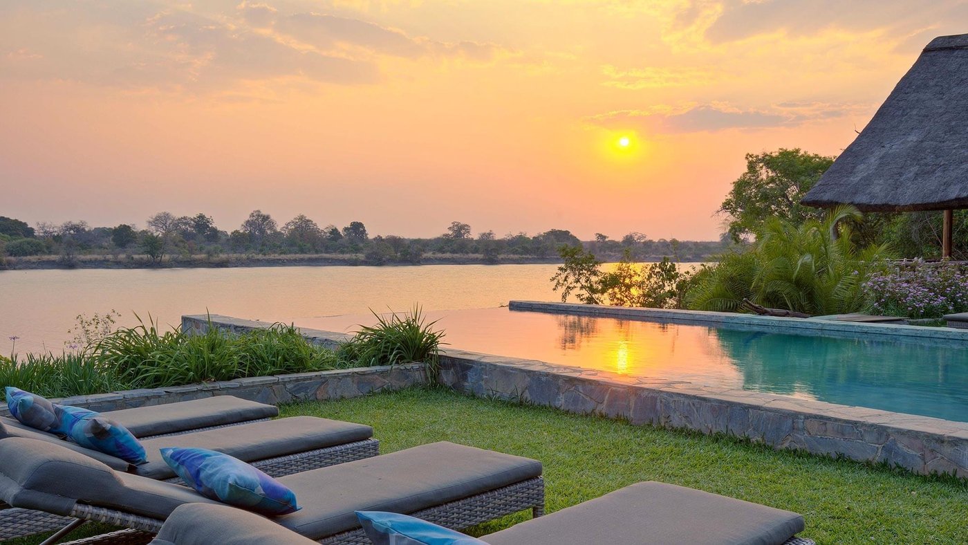 Loungers line the pool deck overlooking the river at sunset at Ila Safari Lodge.