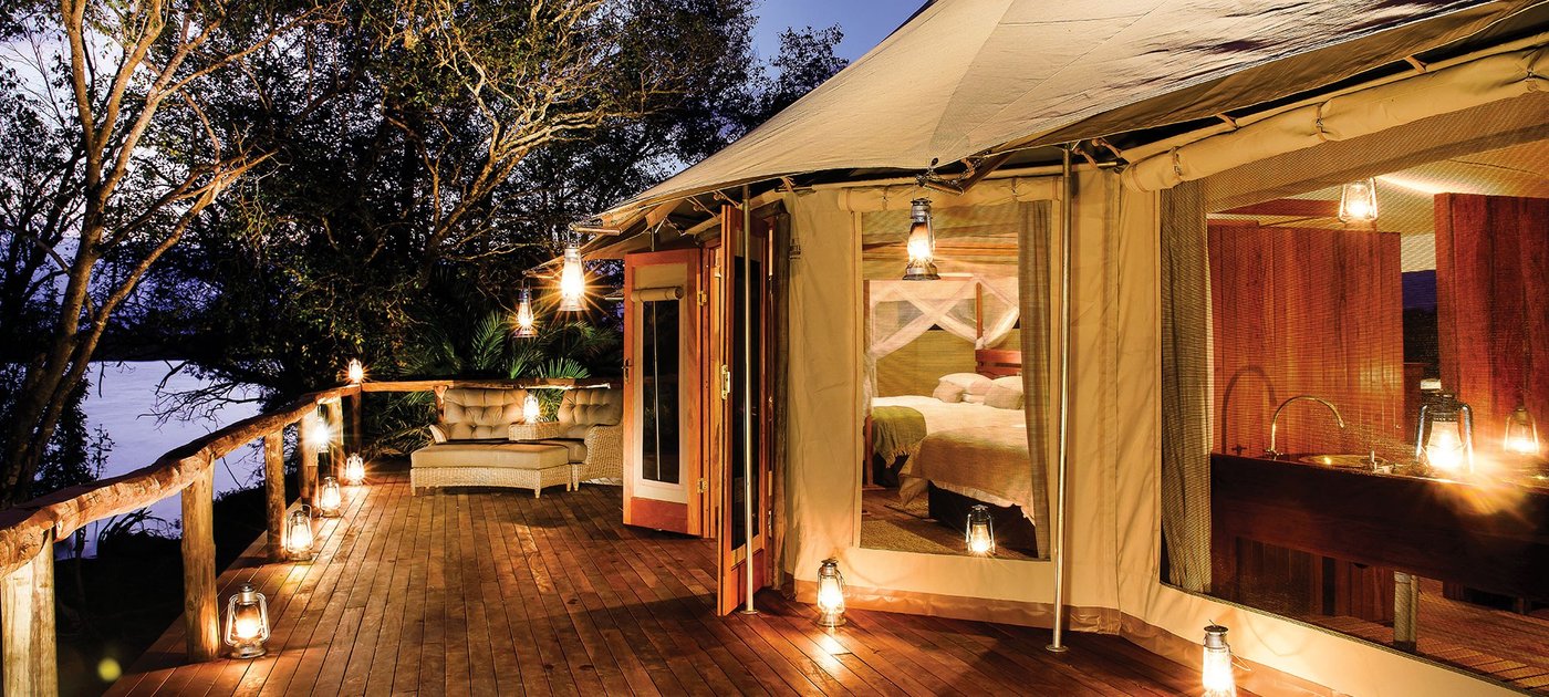 Lantern-lit tented suites line the deck at dusk at Ila Safari Lodge.