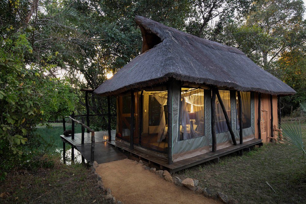 A thatched chalet glows at dusk beside the water at KaingU Safari Lodge in Kafue.