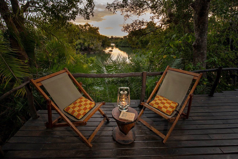 Two deck chairs and a lantern look out over the river at KaingU Safari Lodge.