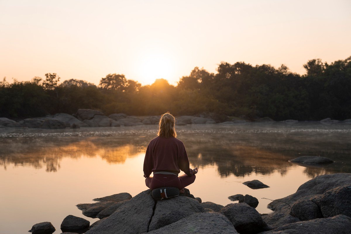 A guest sits in meditation on a rock by the river at Kasabushi Camp.