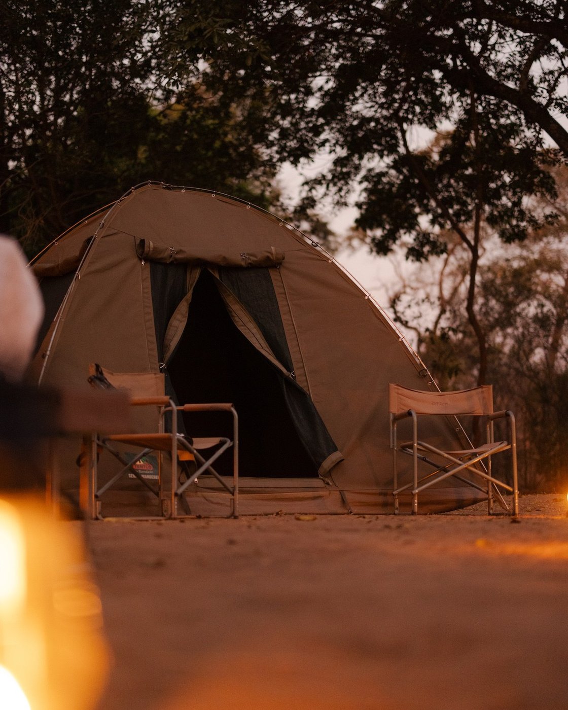 A dome tent and camp chairs glow by firelight at Kasabushi Camp.