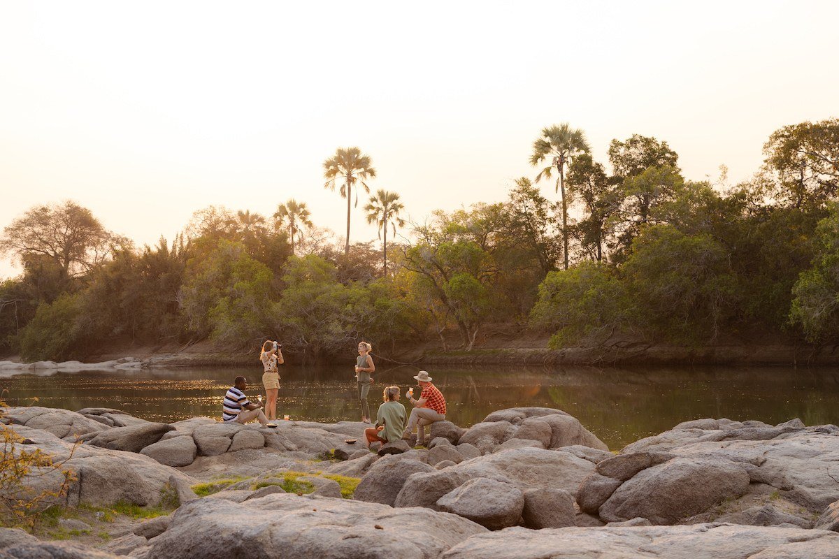 Guests gather on riverside rocks at sunset at Kasabushi Camp.
