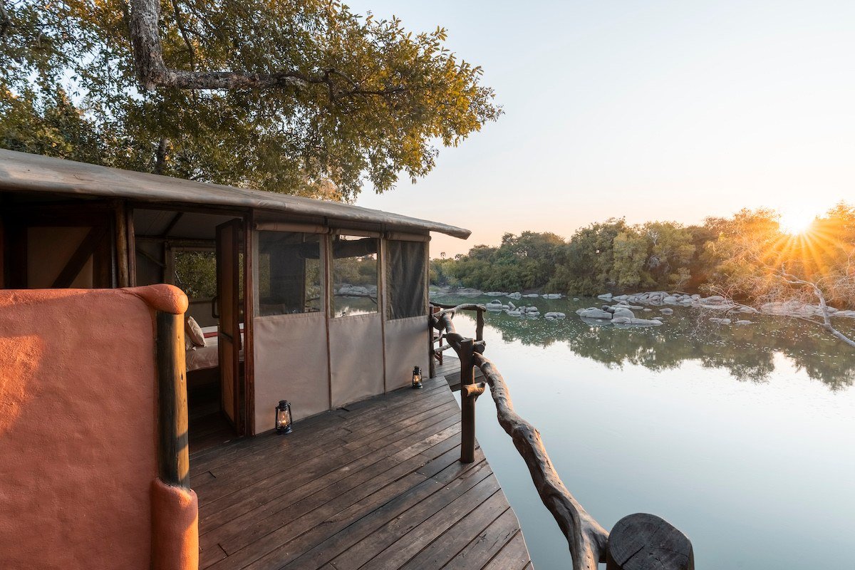 Stilted chalets stand over the river at sunset at Kasabushi Camp.