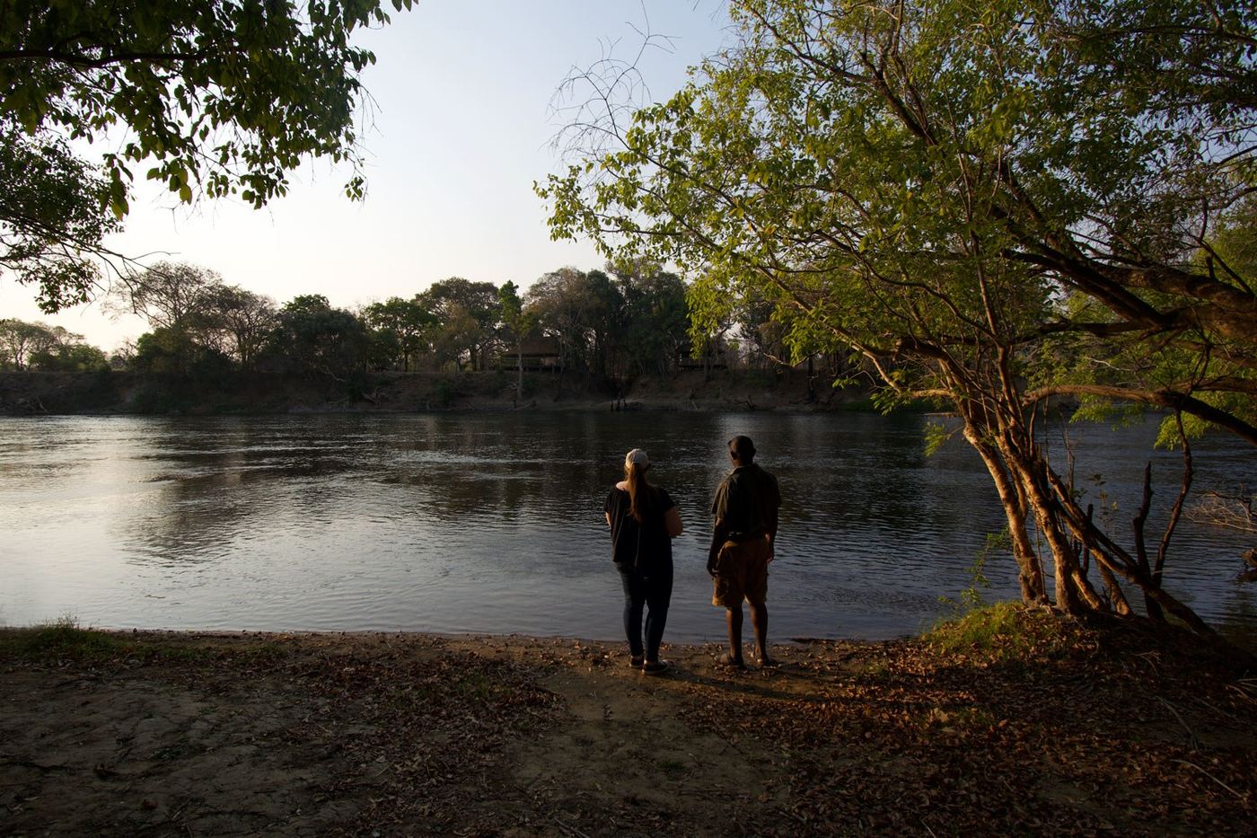 Still water mirrors the trees along the river at Lunga Kikuji Camp.