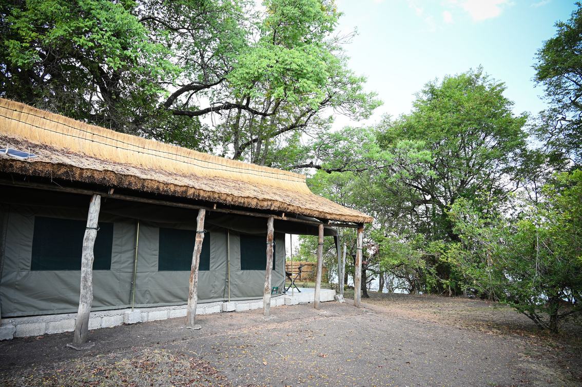 A thatched tent with a wide porch sits among trees at Mapunga Bush Camp in Kafue.