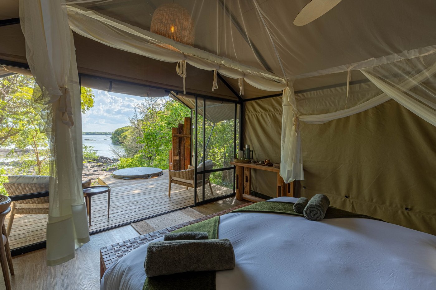 A tented suite bed faces glass walls overlooking the river at Mawimbi Bush Camp.