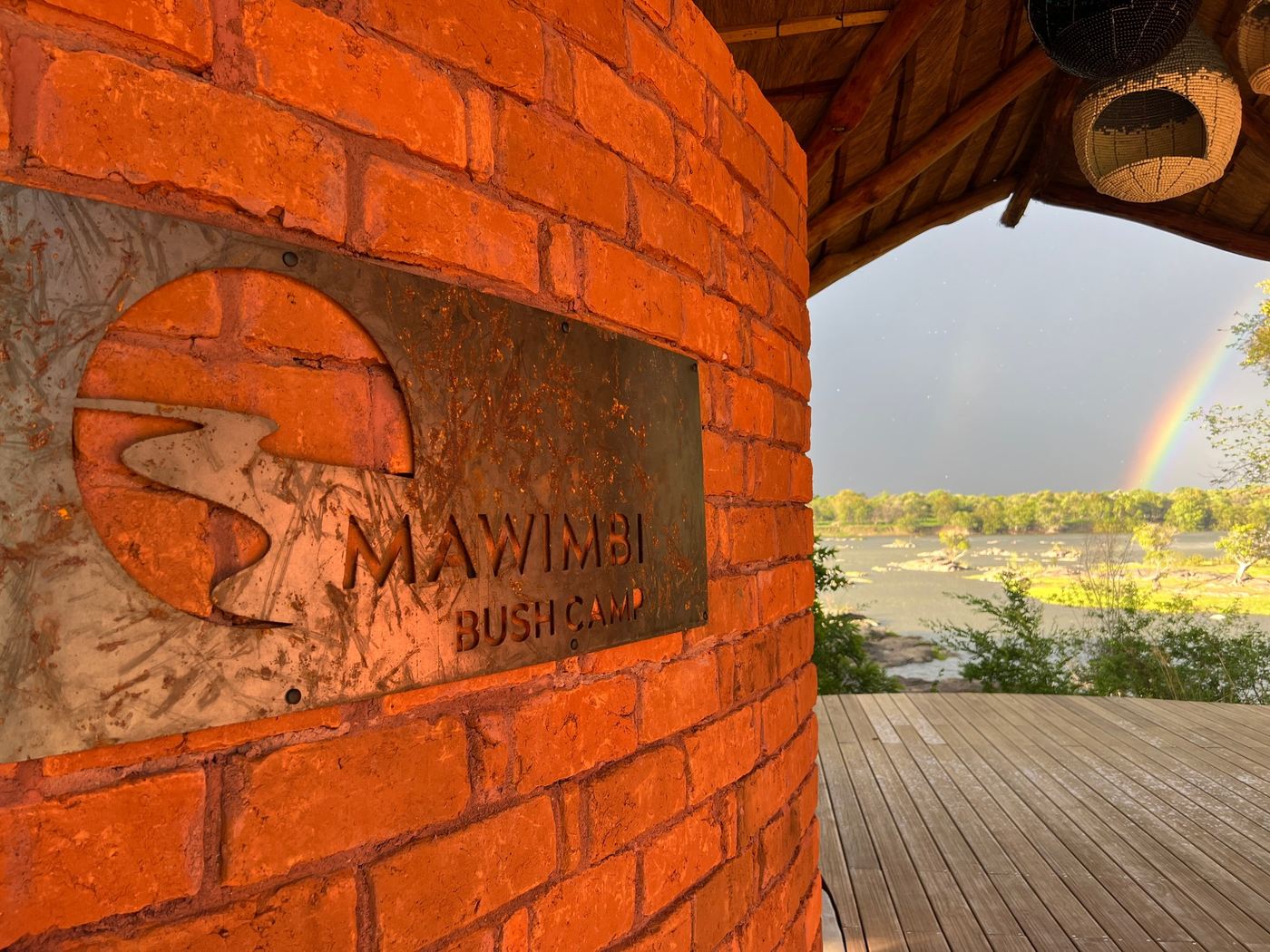 A rainbow arcs behind the brick signboard at Mawimbi Bush Camp.