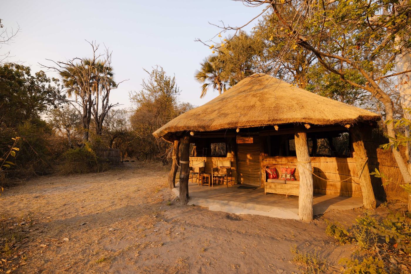 A thatched lodge building stands among trees at McBrides' Camp in Kafue.