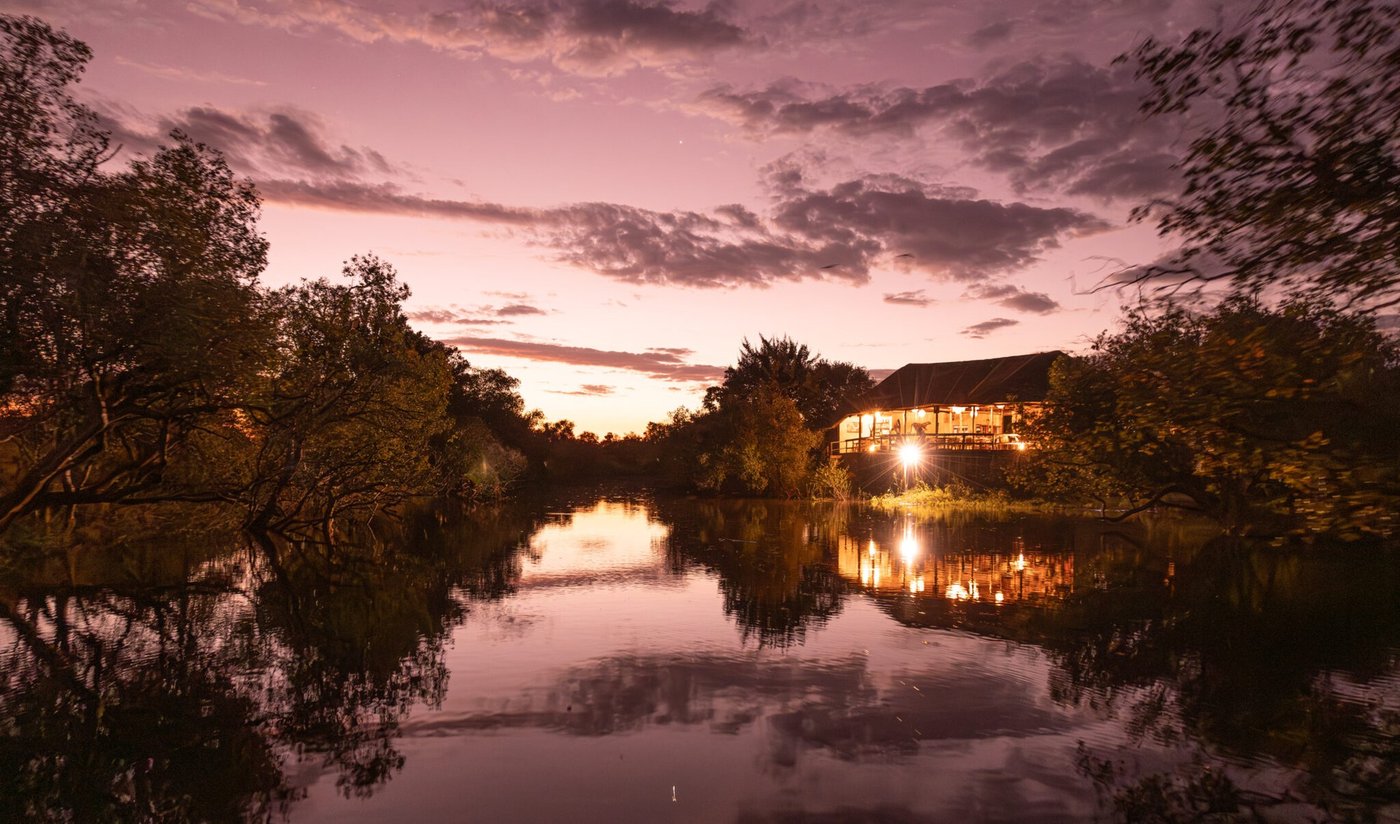 Lodge lights reflect on still water at dusk at Mozhi Bush Camp in Kafue.