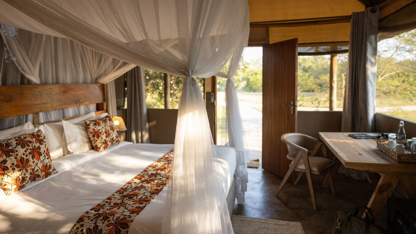 A canopy bed sits beside open doors in a tented suite at Mozhi Bush Camp.