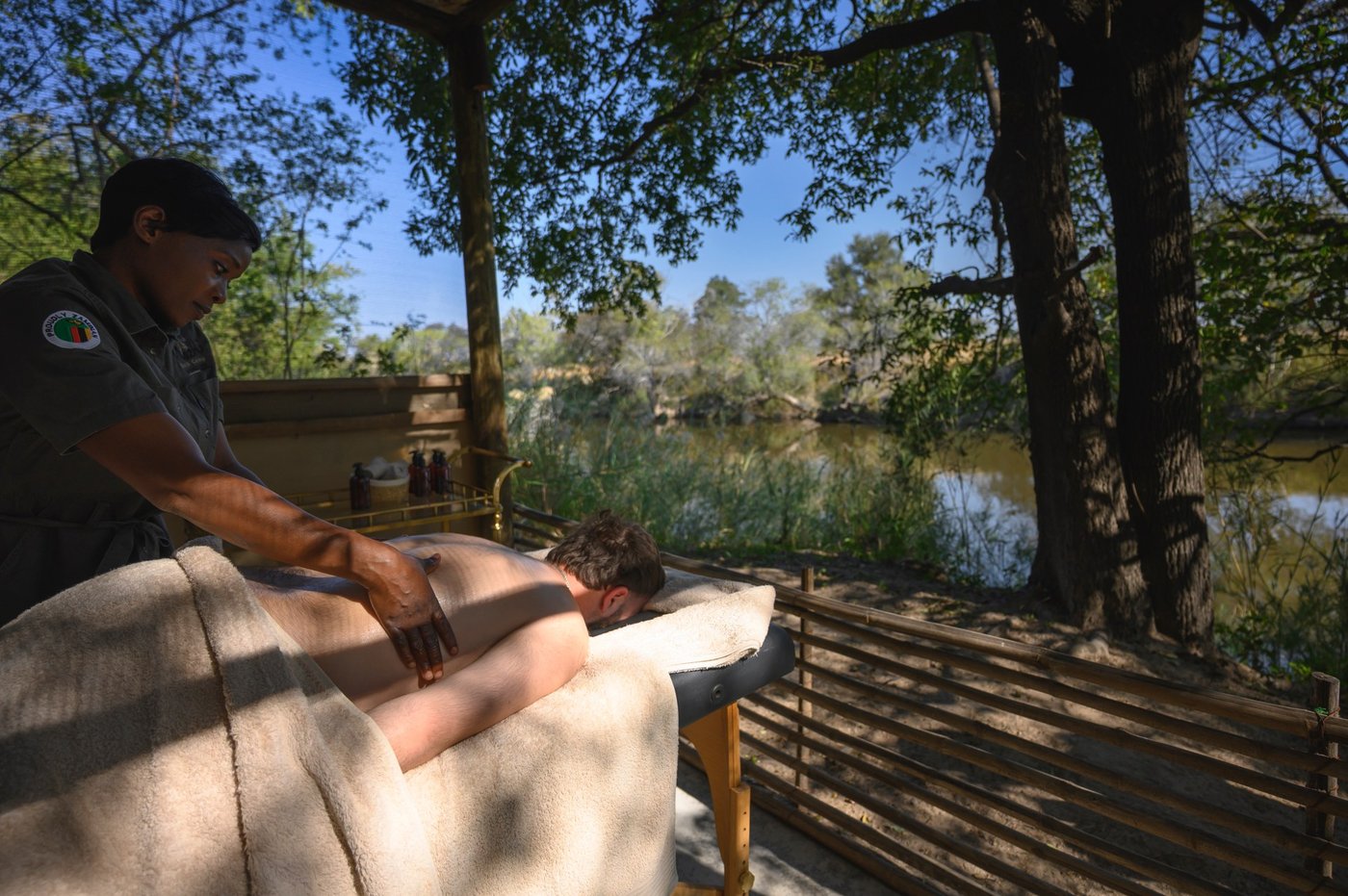 A guest receives a massage on a deck beside the river at Mozhi Bush Camp.
