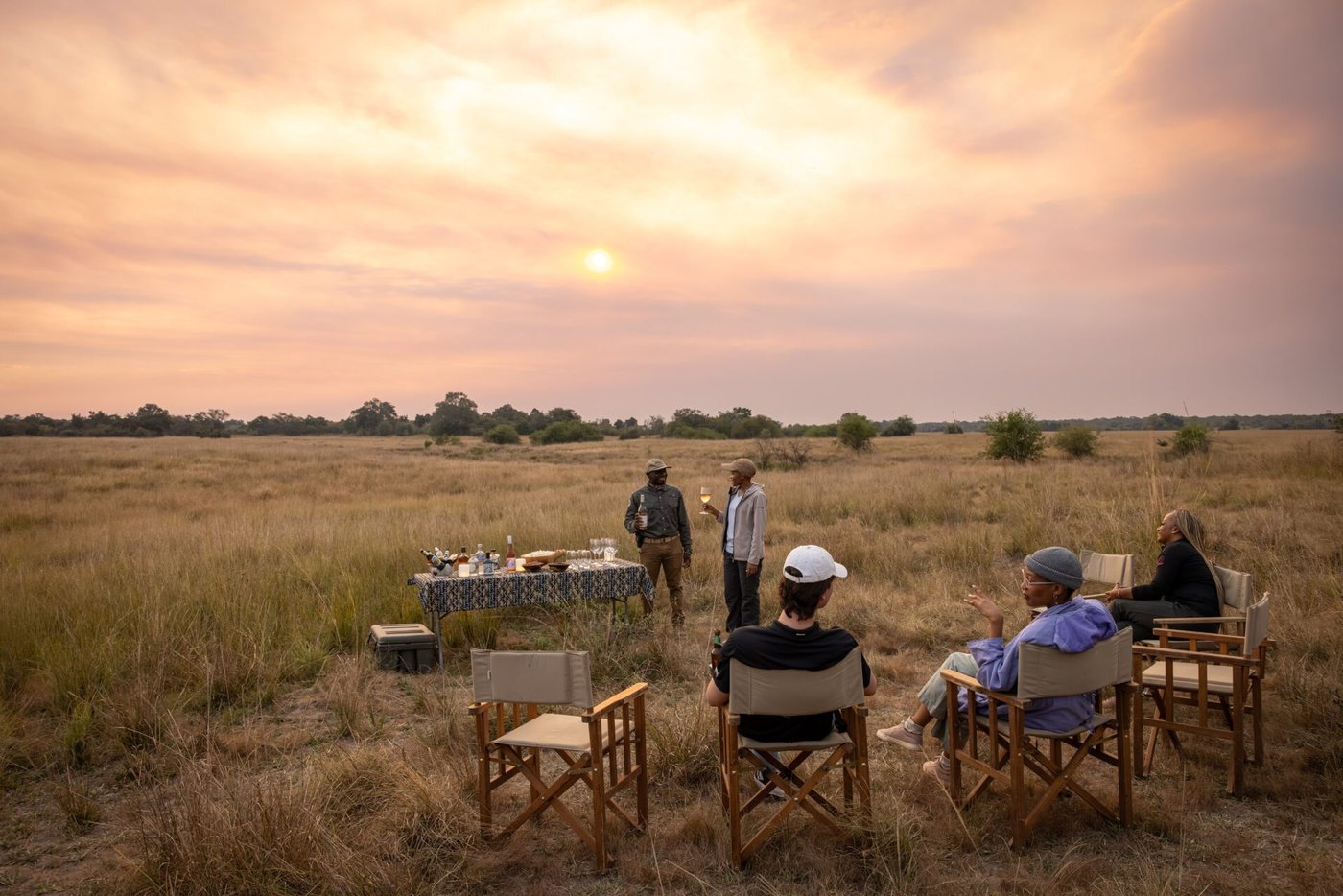 Guests dine at a table set on the plains at sunset at Mozhi Bush Camp.