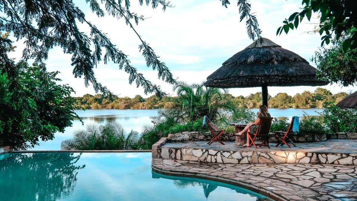 A guest relaxes under a thatched umbrella beside the pool at Mukambi Safari Lodge.