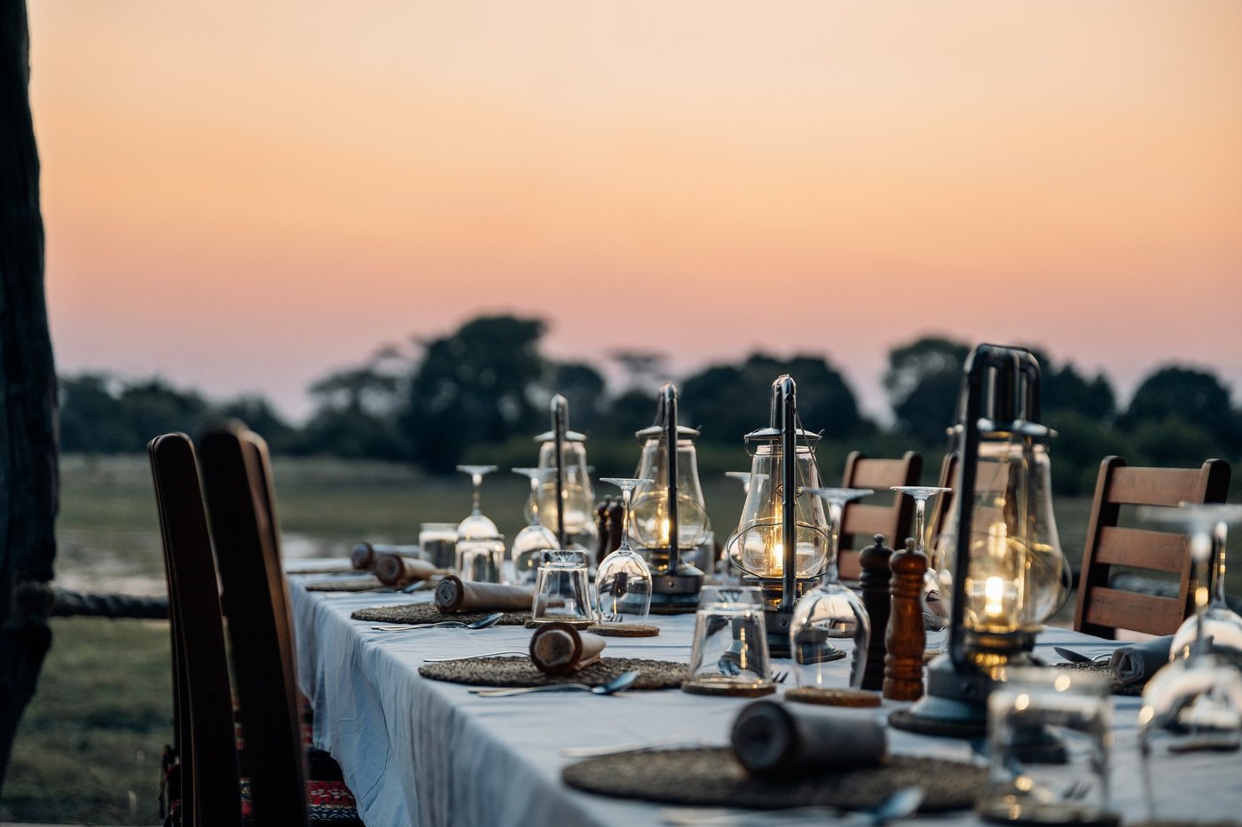 A dining table is set for sunset under the trees at Musekese Camp.