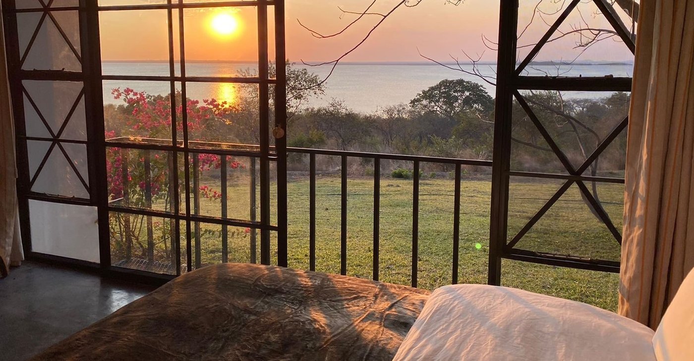 A bedroom opens to a balcony with a lake sunset at Musungwa Safari Lodge.