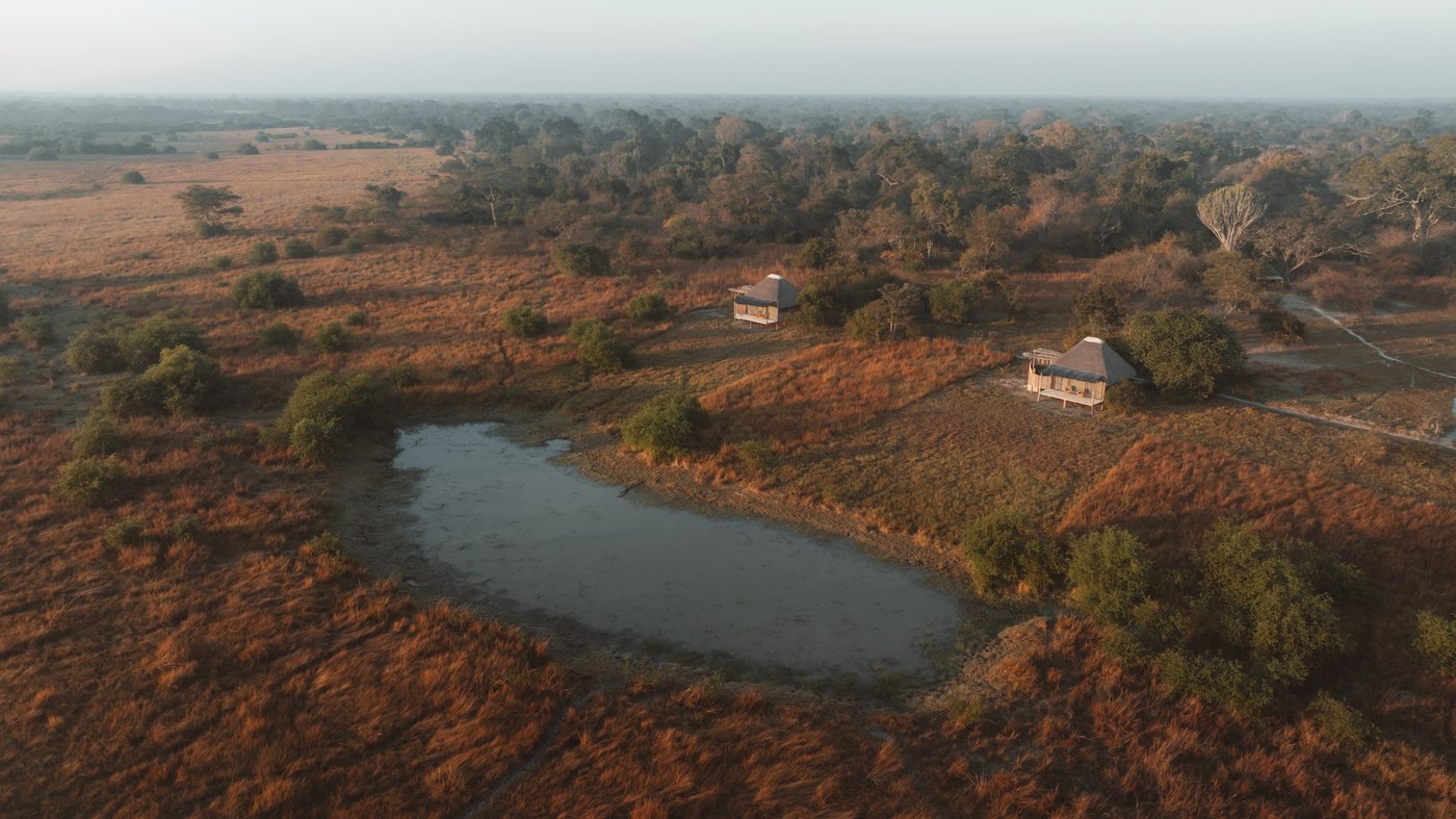 An aerial view shows Ntemwa-Busanga Camp among trees beside a plains lagoon in Kafue.